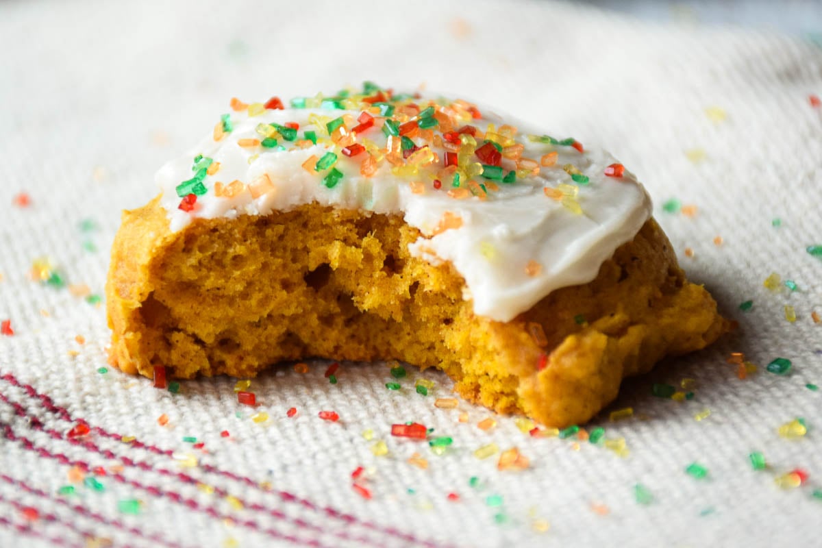 Frosted soft pumpkin cookie with fall colored sprinkles and a bite taken out of it.