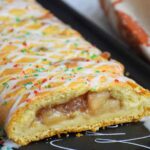 Up close image of cut caramel apple cheese danish on a black tray.