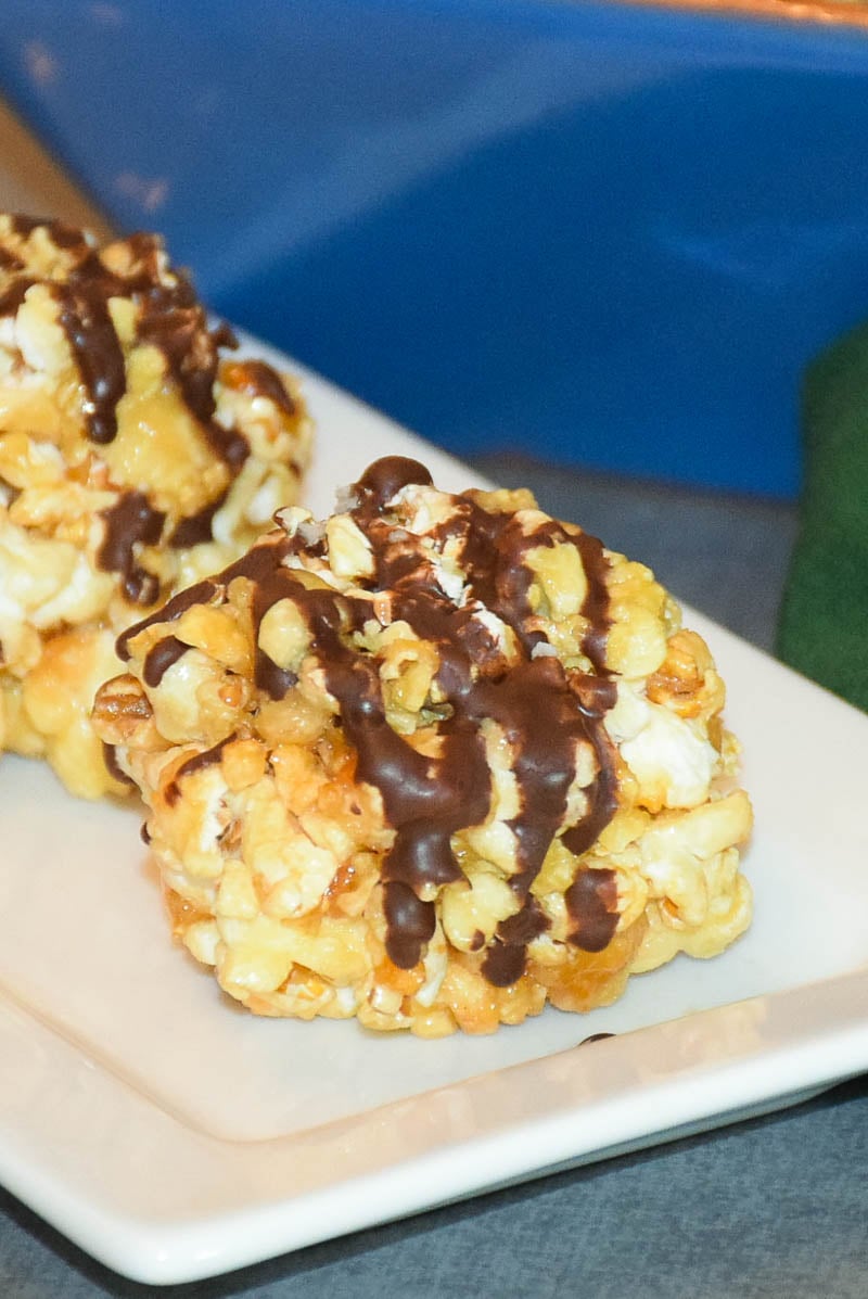 Honey Popcorn Ball drizzled with dark chocolate and sea salt on a white plate.