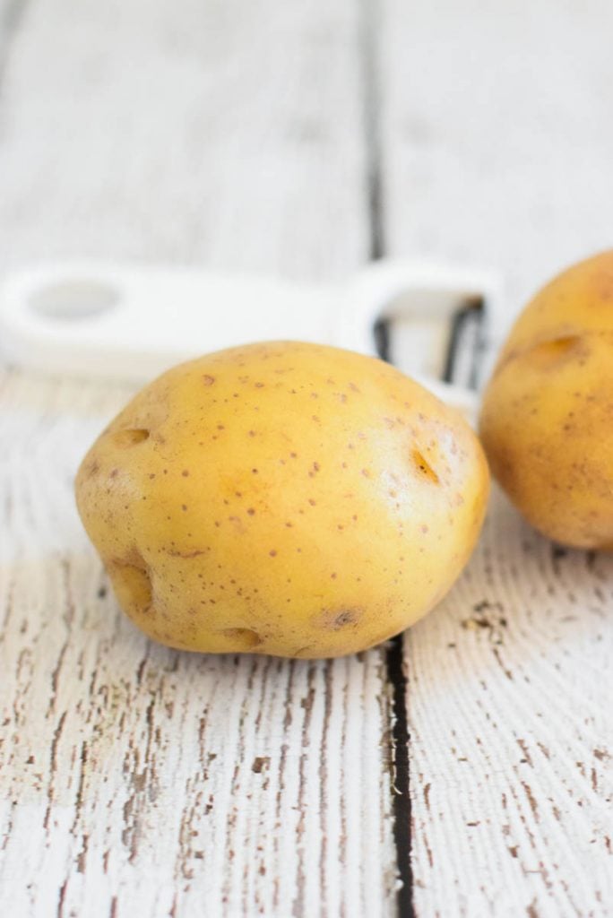 whole gold potato with potato peeler in background