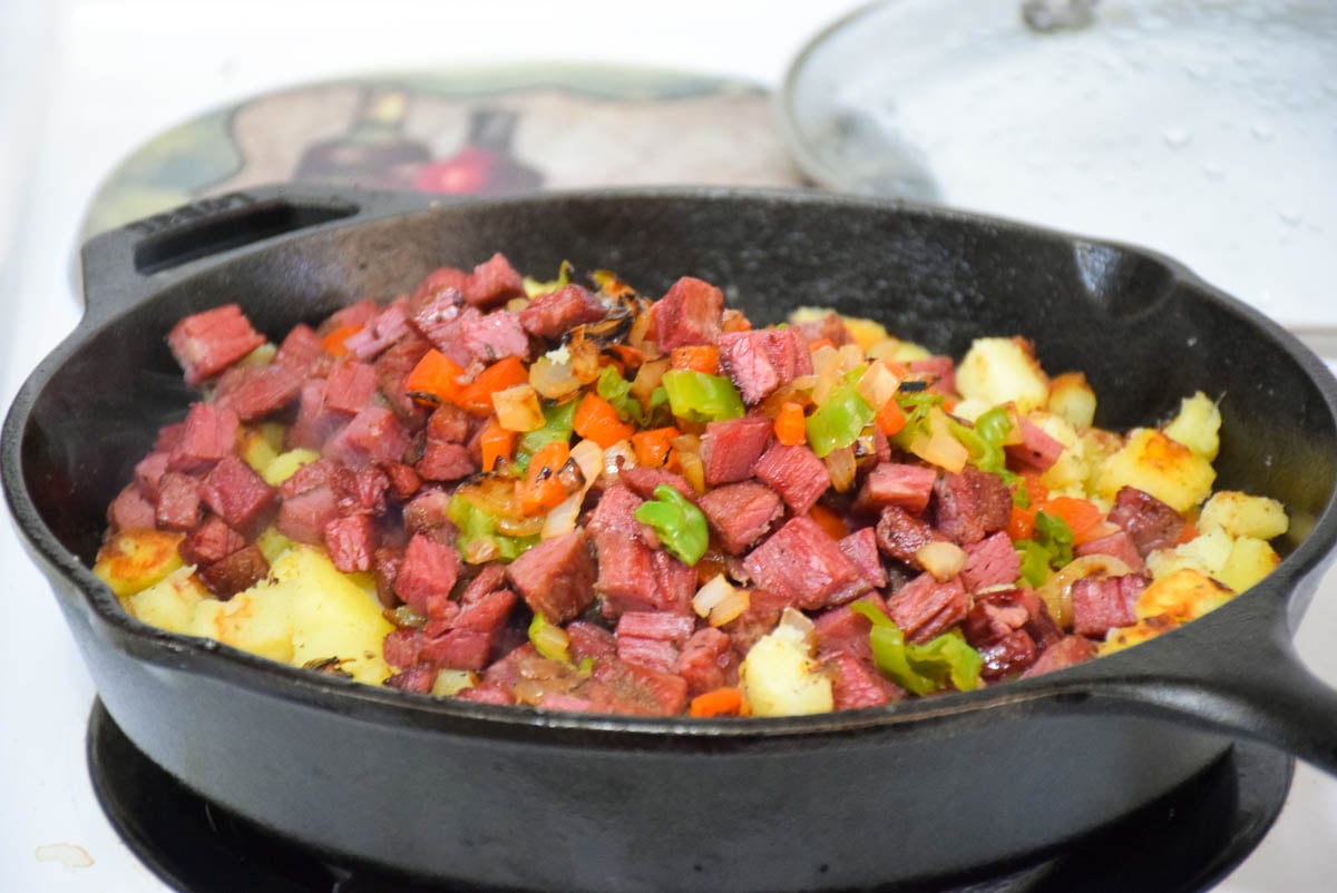 Corned Beef Hash ingredients in a cast iron skillet on the stove top.