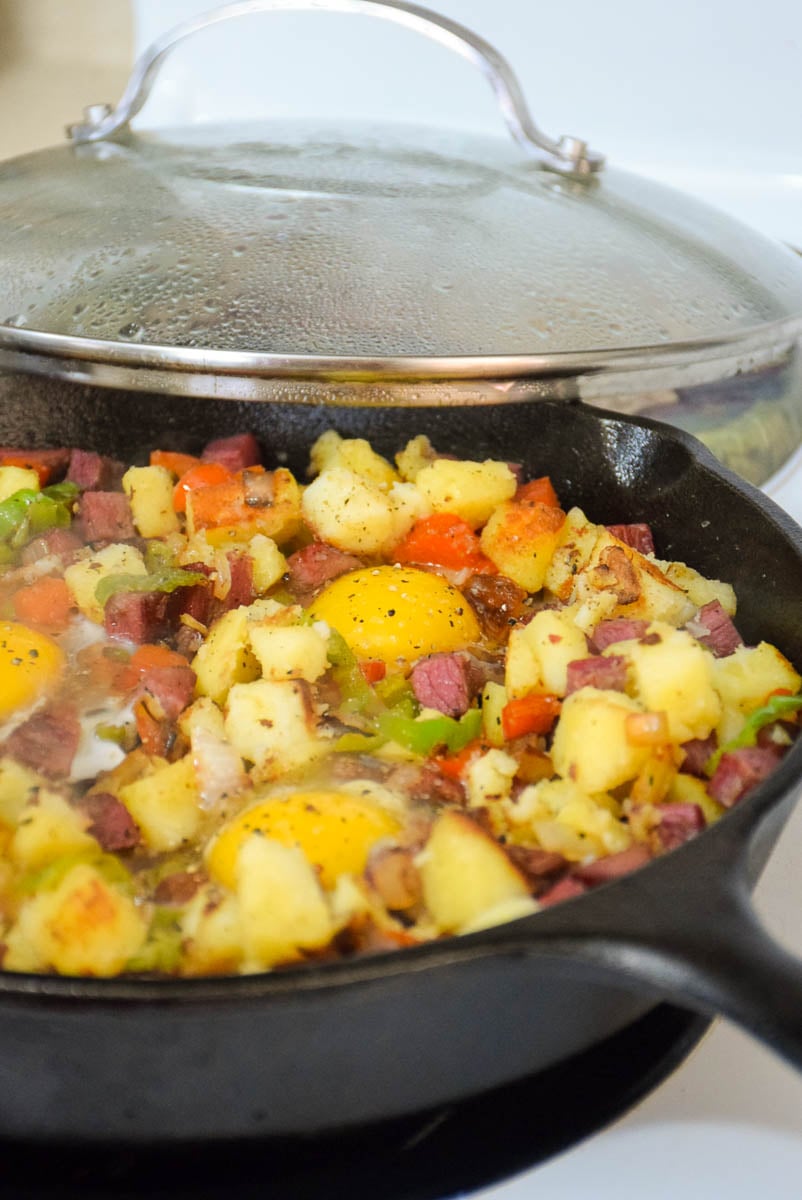 Eggs added to corned beef hash in the skillet for poaching.