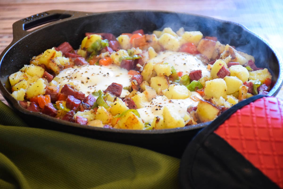 Cooked Homemade Corned Beef Hash and Eggs with steam coming out of hot cast iron skillet.