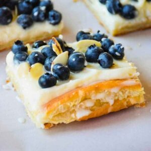A rectangular slice of blueberry almond tart with a creamy white filling, topped with fresh blueberries and sliced almonds on a flaky puff pastry crust.