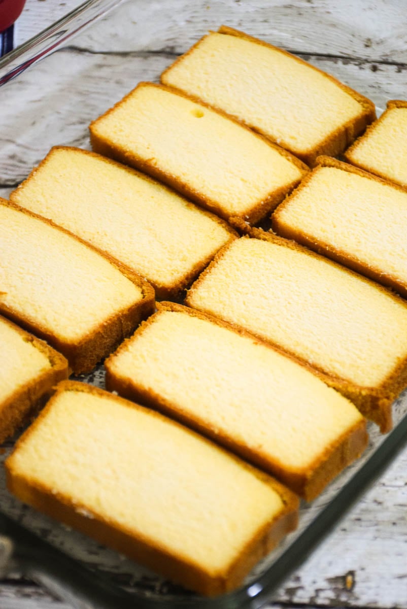 Pound cake slices in the bottom of a glass cake dish.