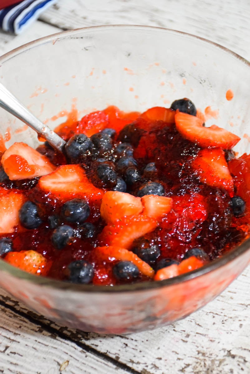 Gelatin with blueberries and strawberries in a clear glass bowl.