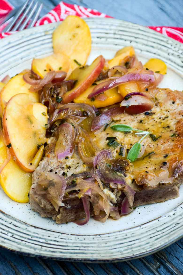 Vertical Image of Skillet Pork Chops with Apples and Onions on serving plate with red and white napkin