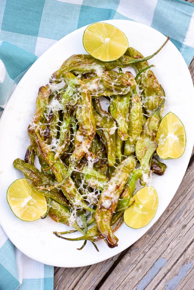 Air fried peppers on a plate with lime wedges.