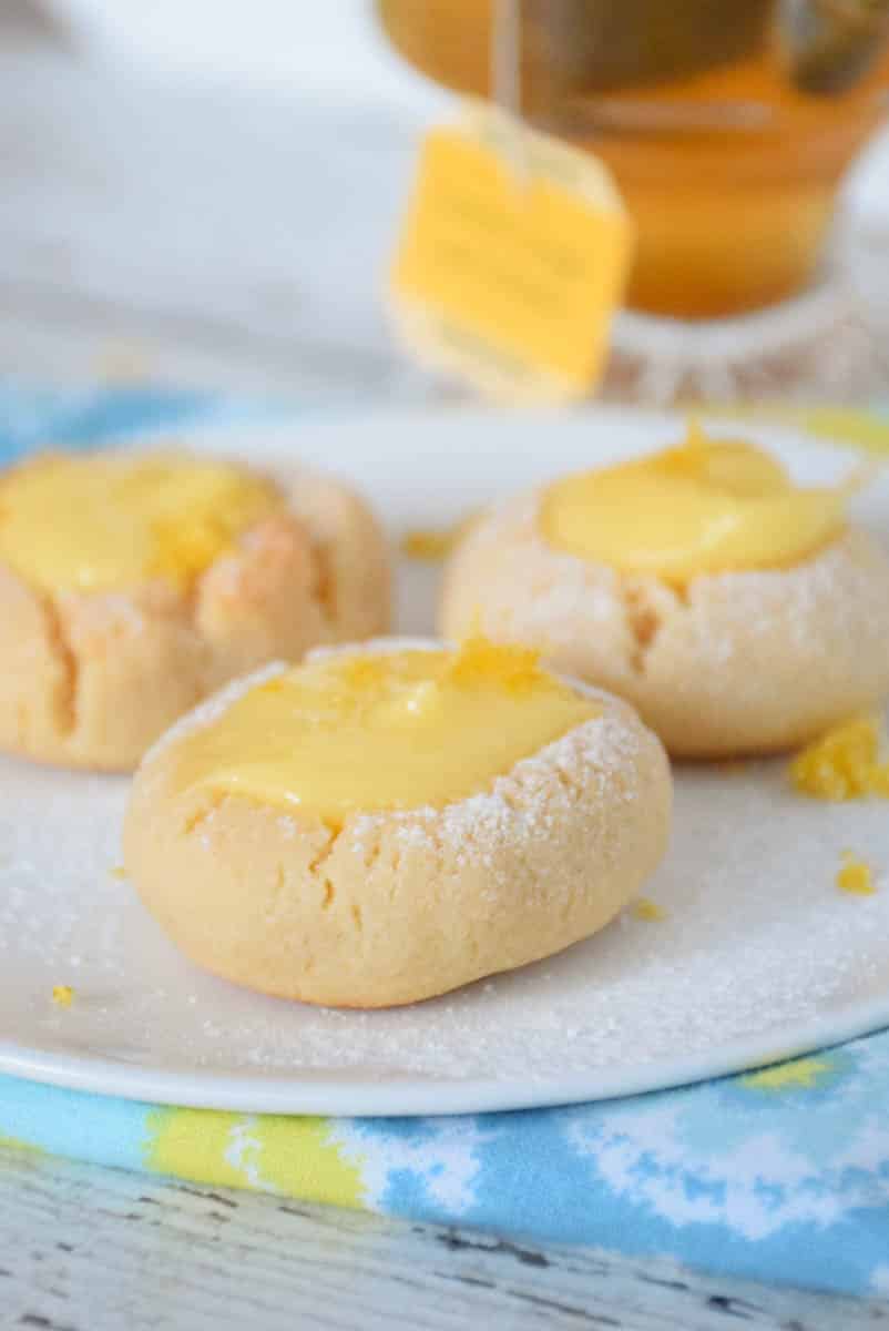 A white plate with lemon curd thumbprint cookies sprinkled with powdered sugar and lemon zest.