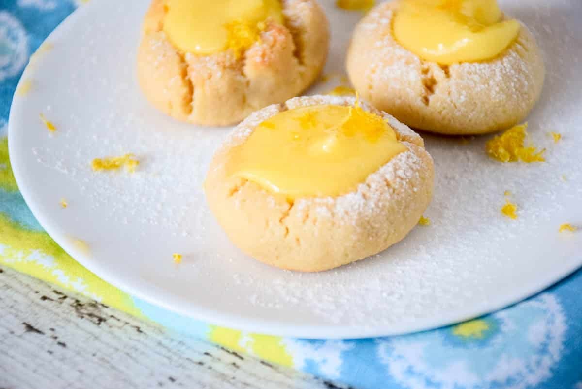 Low Carb Lemon Curd Thumbprint Cookies on a white plate sprinkled with powdered sugar and lemon zest.