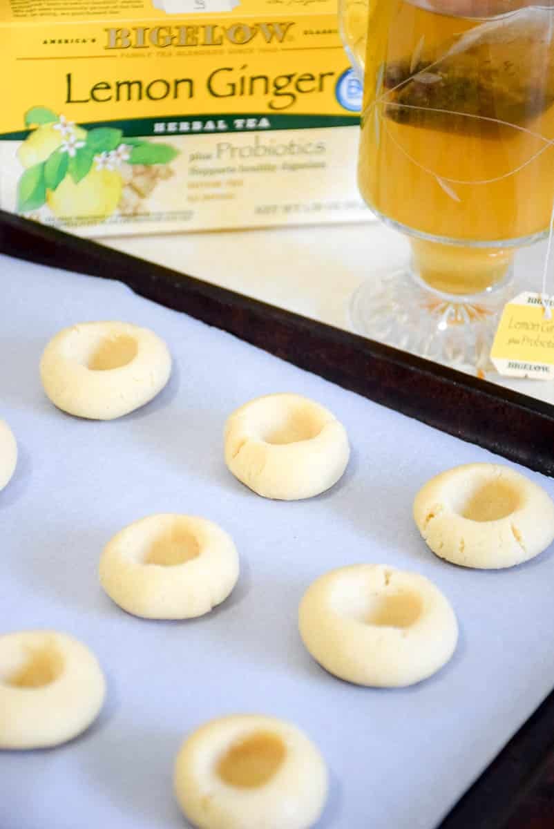 Shortbread cookie dough rolled into a ball with a dent made in the center of the dough on parchment paper lined baking sheet.