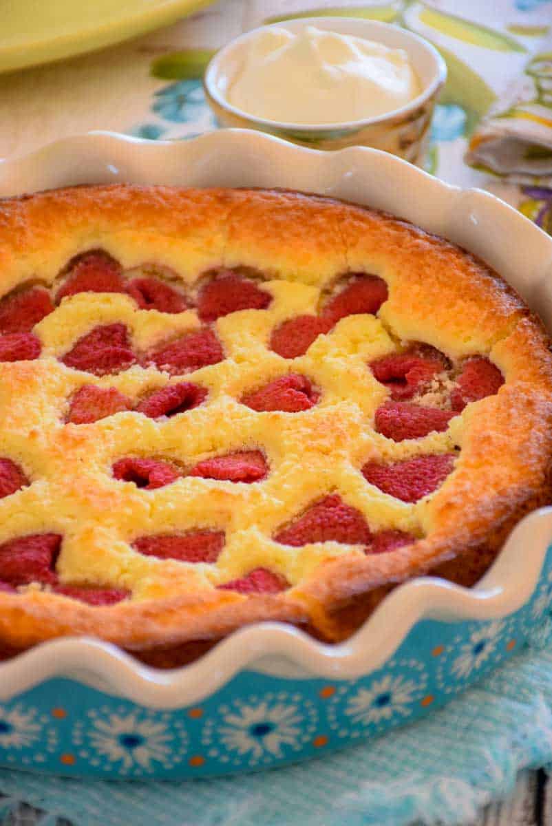 An up close image of a round blue flowered baking dish containing a golden brown keto raspberry coffee cake studded with fresh raspberries.