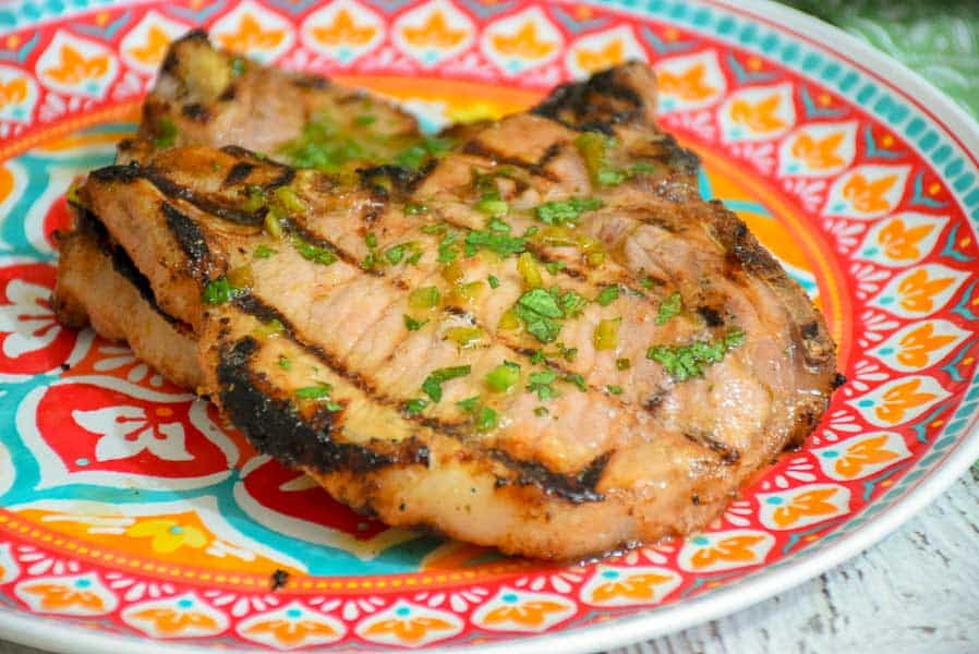 Two grilled pork chops on a plate topped with flecks of cilantro and jalapeno.