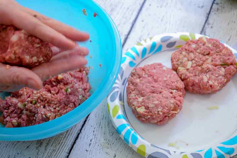 A pair of hands shaping ground beef into hamburgers 2 formed burgers on a plate