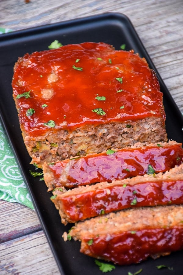 Cooked spicy meatloaf on a black tray with cut slices.