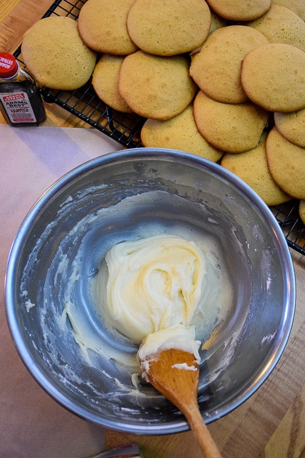 Buttercream frosting in a bowl with a stack of cookies behind the bowl.