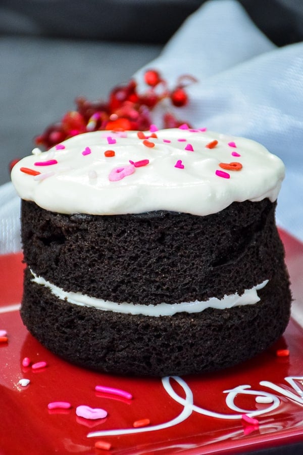 Two layer keto chocolate mug cake with whipped cream in the middle layer and on top of the cake with red and pink heart sprinkles on top.