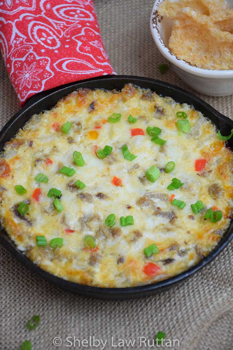Baked Philly Cheesesteak Dip topped with green onions, served in a cast iron skillet with pork rinds on the side.