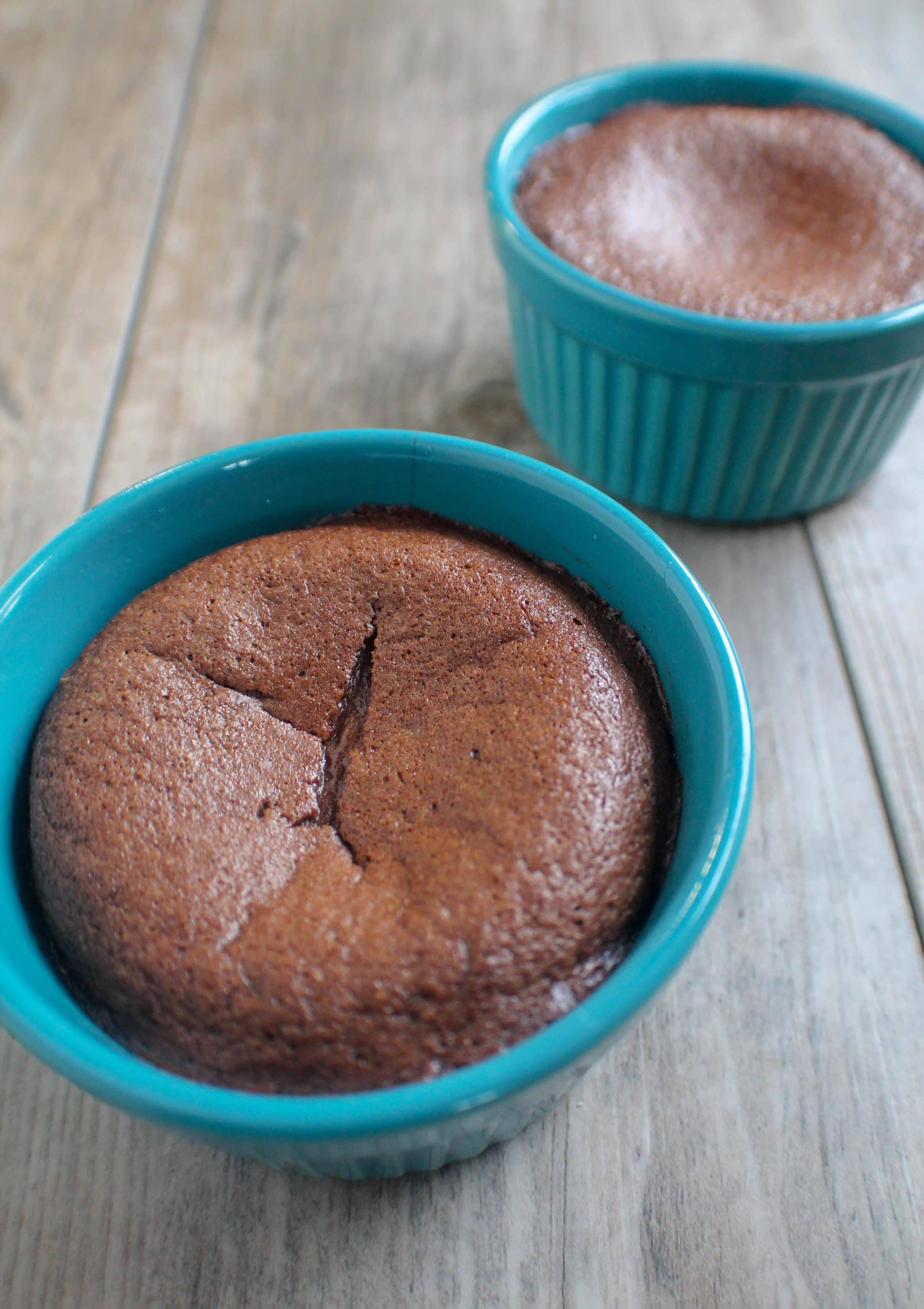 Freshly baked keto chocolate pudding cake in a blue ramekin, showing a cracked top and a soft, molten center.