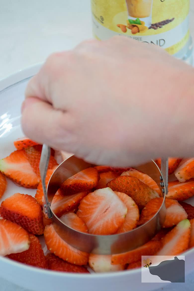 Sliced berries in bowl being chopped by hand with biscuit cutter.