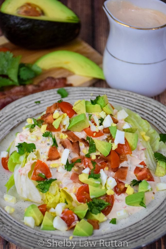 Thousand Island Salad Dressing on an iceberg lettuce wedge with tomatoes, bacon, hard boiled egg, avocado, and cilantro