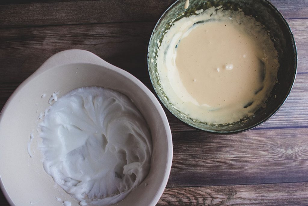 Two bowls, one with whipped egg whites and other with combined egg yolk mixture. 