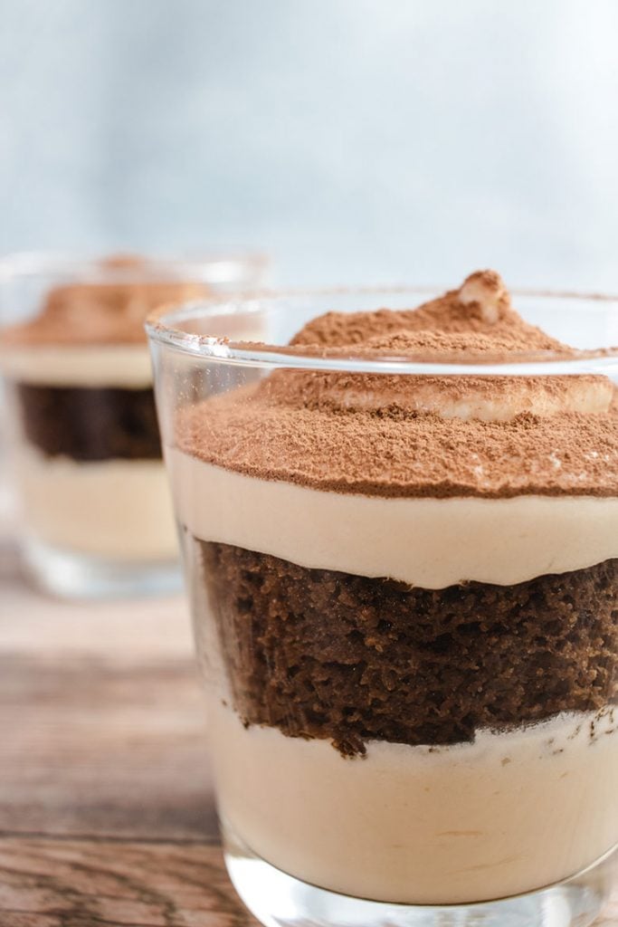 Keto tiramisu in a small drinking glass with another keto tiramisu in the background.