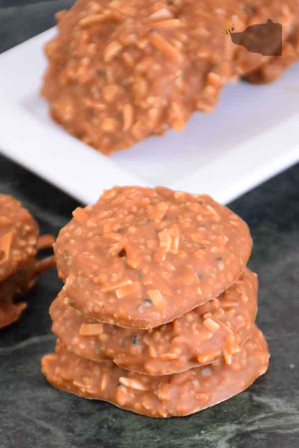 stack of 3 keto no bake cookies on green marble board with more cookies on a white plate in the background