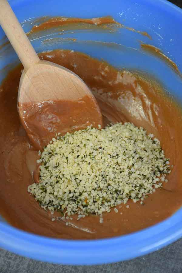 blue mixing bowl with peanut butter mixture and hemp seed ingredient in bowl ready to mix in