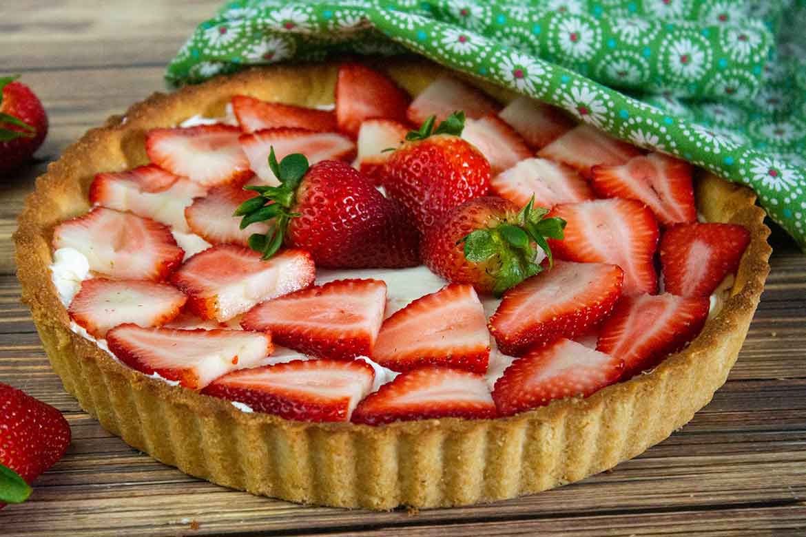 A cookie tart crust filled with almond cream cheese filling and beautifully arranged strawberry slices on top