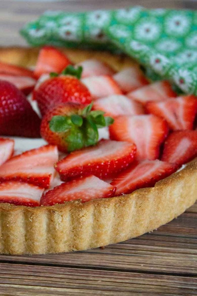 One half of a Strawberry Tart with sliced berries on top and a green and white napkin in the background