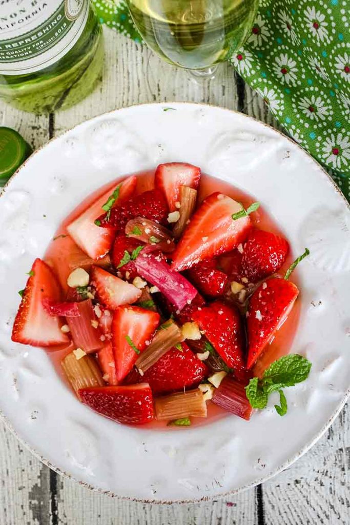 Overhead view Strawberry Rhubarb Salad on a seashell plate with sauvignon blanc bottle of wine and a class of wine poured behind the salad