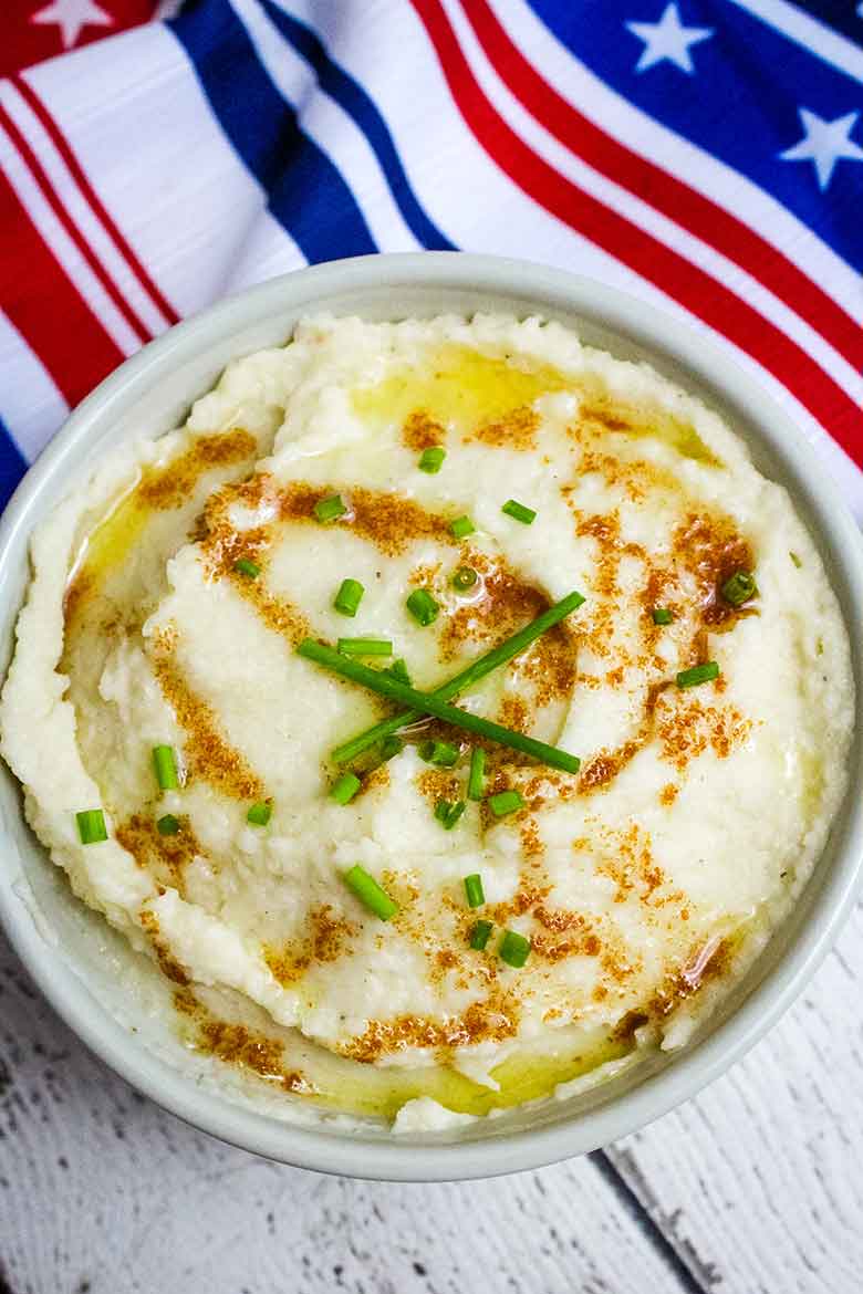 Overhead image of a bowl of garlic mashed cauliflower drizzled with browned butter and garnished with green chives.