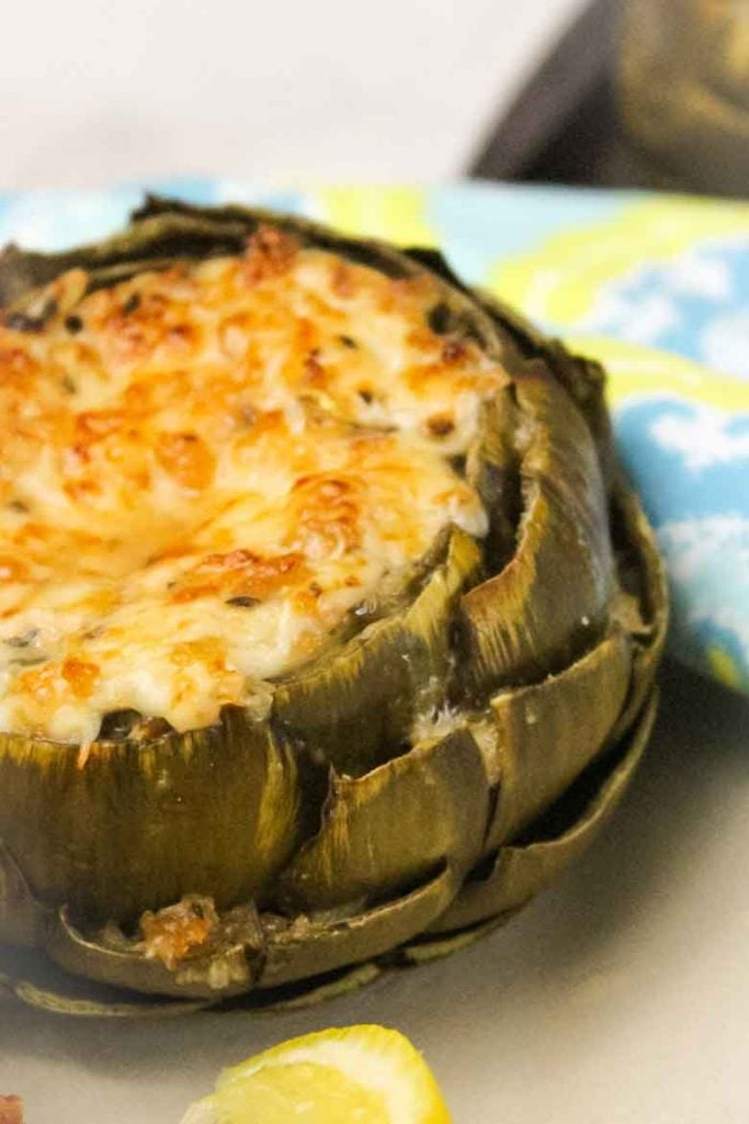 Cheese and Herb Stuffed Artichoke with a lemon wedge