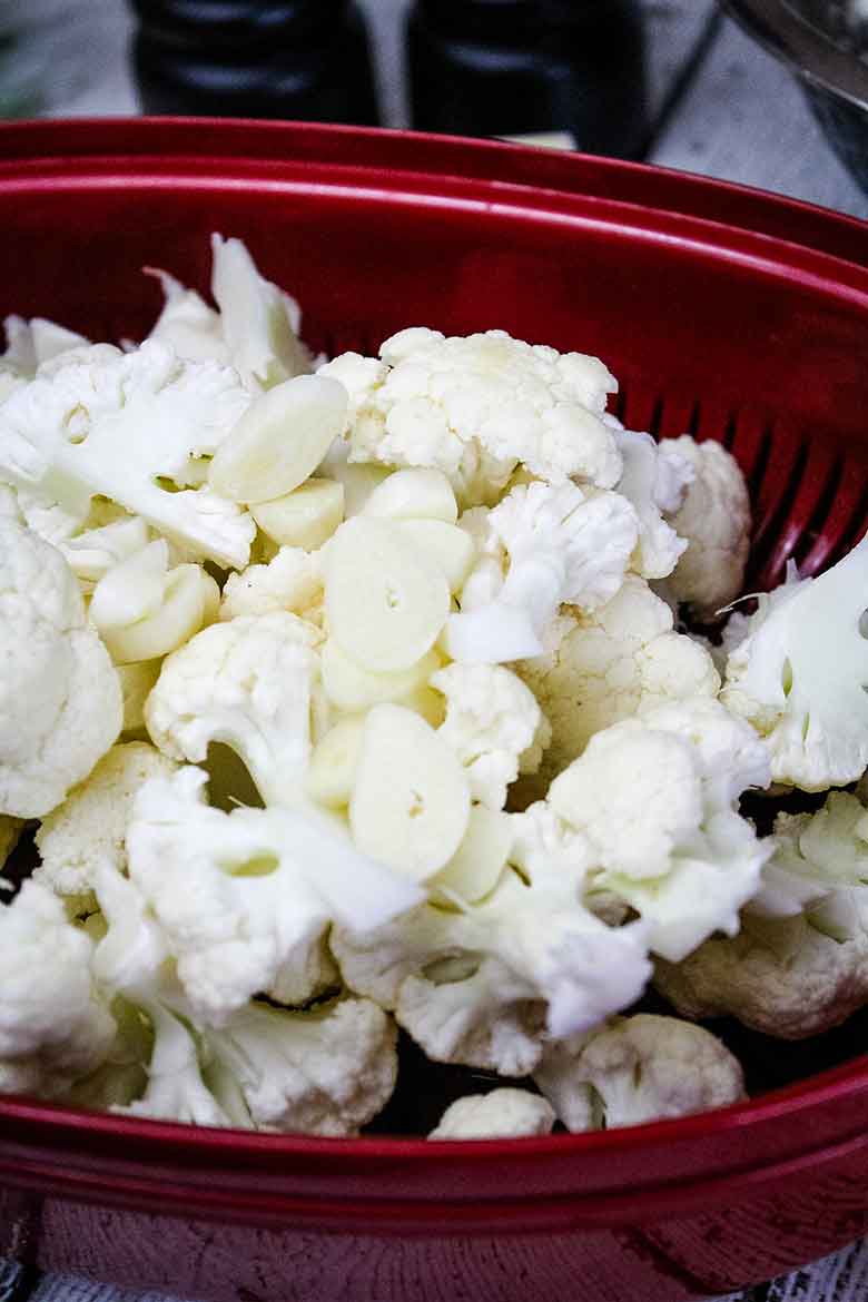 Cauliflower and sliced garlic in a red microwave steamer.