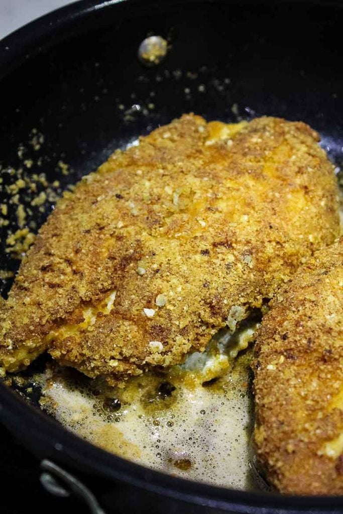 Breaded chicken frying in a large skillet.