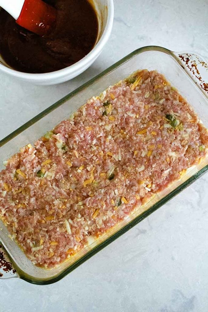 overhead view of meatloaf mixture in loaf pan with ketchup topping next to it