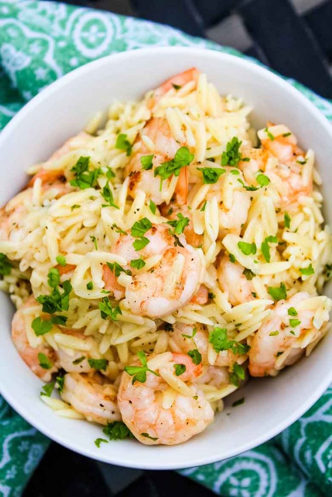 Overhead shot of cooked shrimp and orzo pasta in a bowl sprinkled with green parsley.