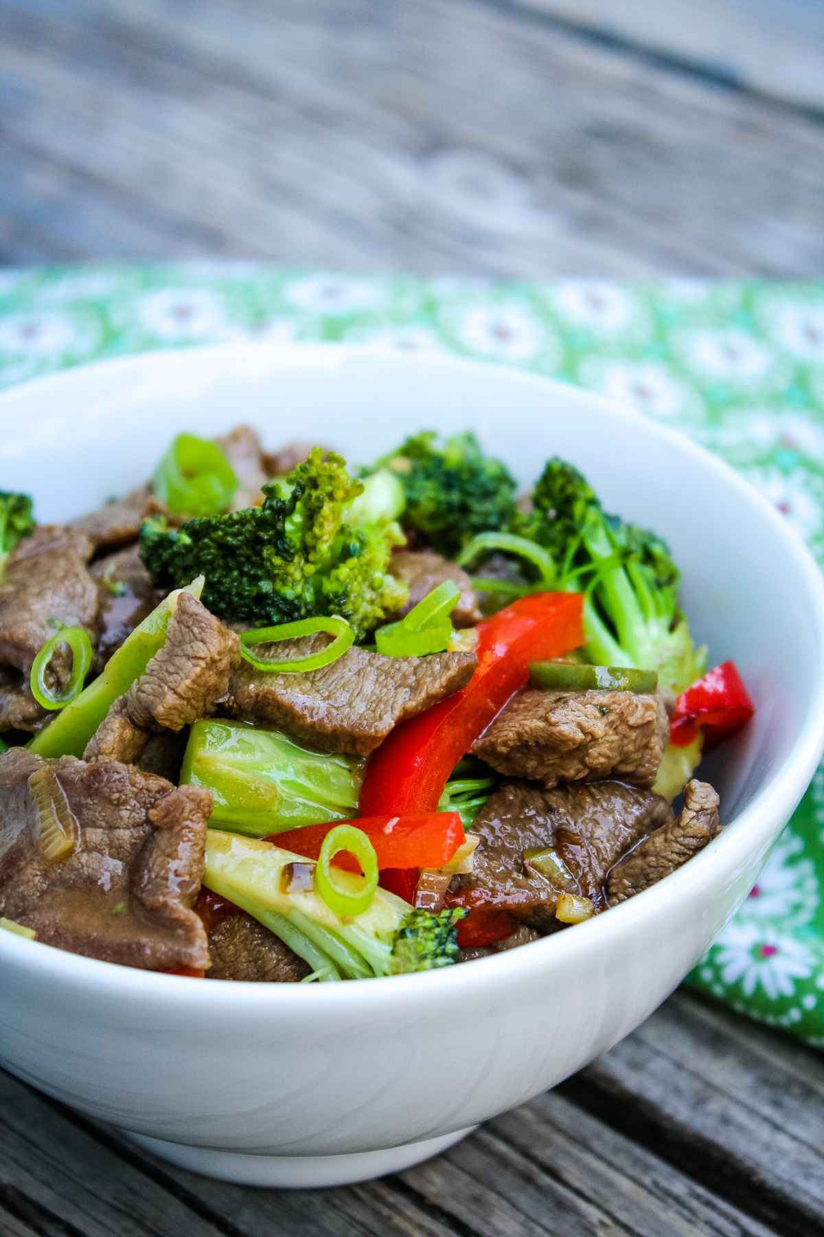 A white bowl full of sweet and spicy vension stirfy  with bright green broccoli, onins, and red bell pepper strips.