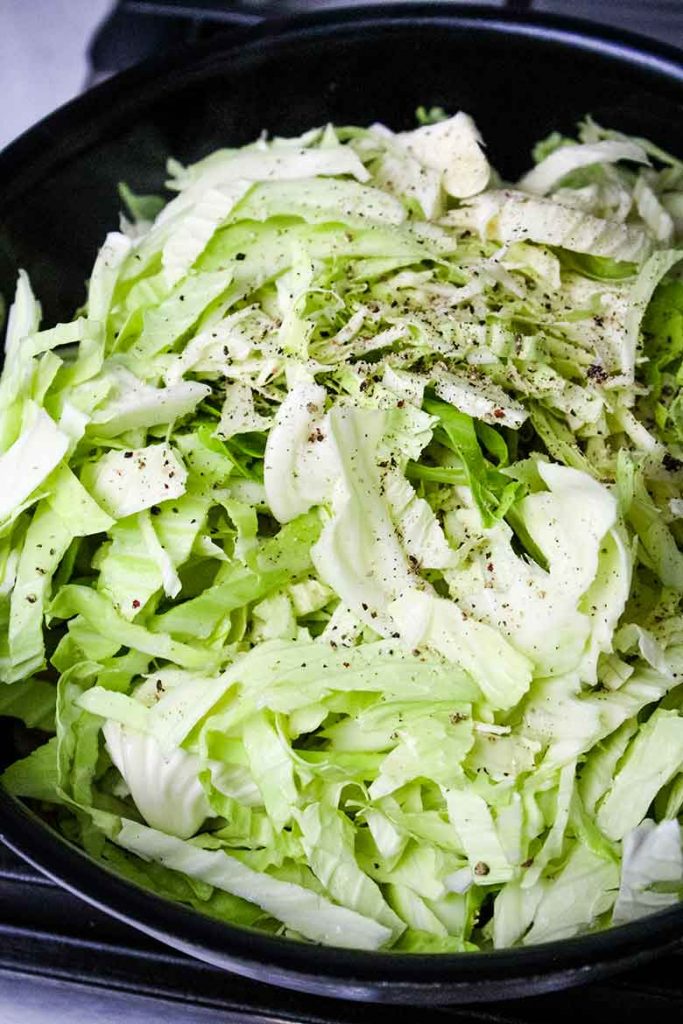 Sliced cabbage in the hot skillet with salt and pepper seasoning sprinkled on top