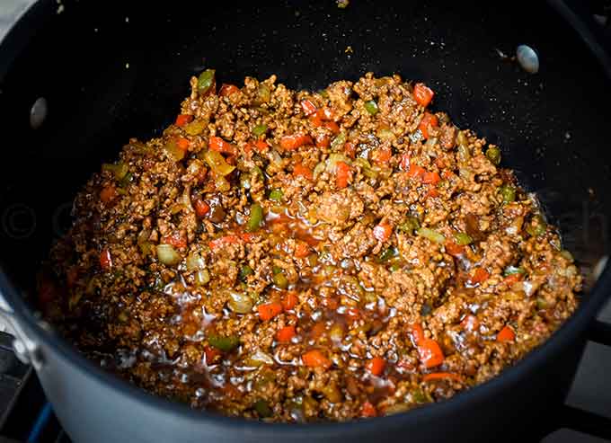 A stock pot with ground beef, seasoning, and vegetables cooking together