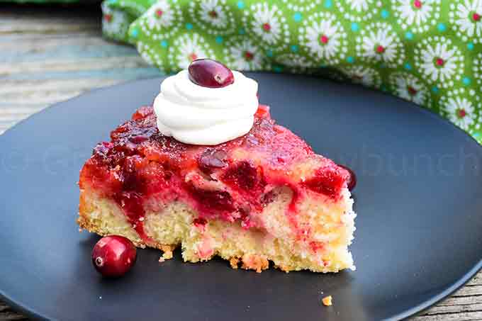 A slice of cranberry upside down cake on a black plate with whipped cream on top