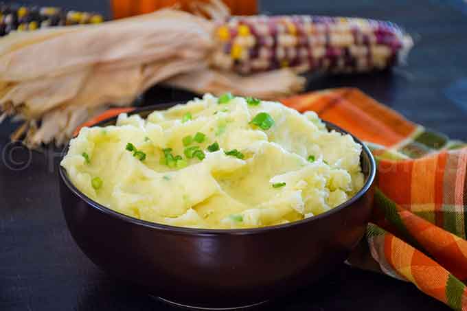 A brown bowl with mashed potatoes topped with chives.