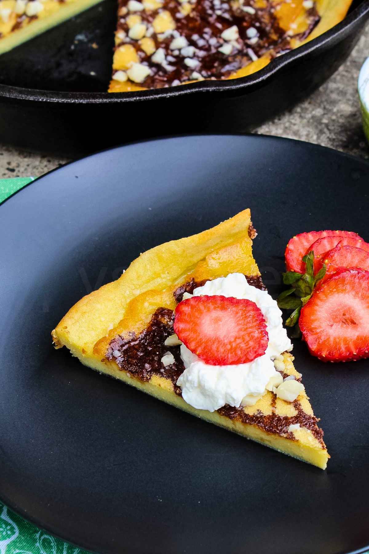 A triangular slice of german pancake topped with whipped cream and strawberries drizzled with chocolate and macadamia nuts.