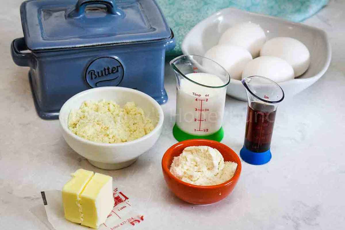 A variety of low-carb baking ingredients like almond flour, eggs in a bowl, and a stick of butter arranged on a white counter.