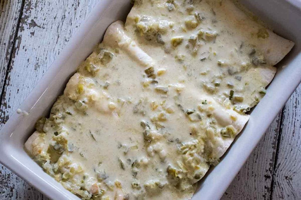 Assembled green chicken enchilada recipe covered with green sauce ready to bake.