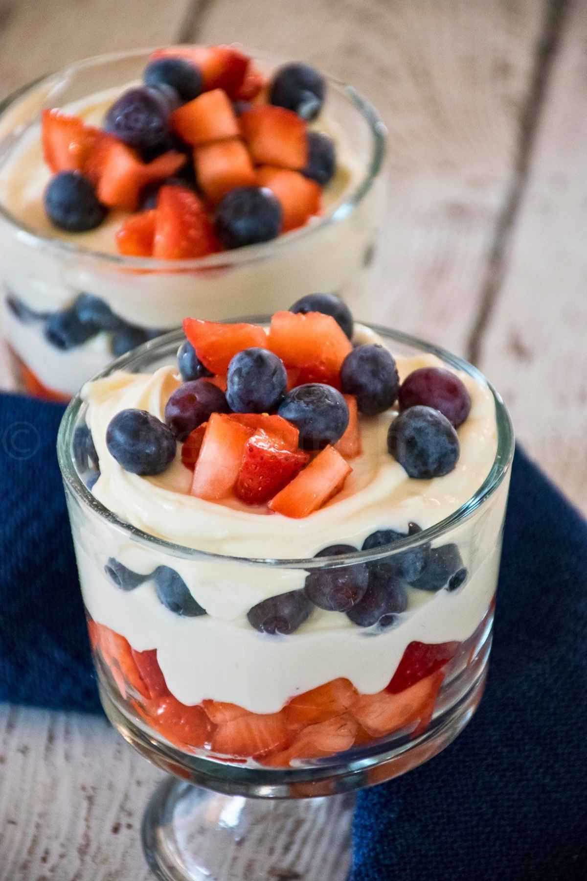 Glass parfait dishes filled with layers of creamy cheesecake, fresh blueberries, and diced strawberries.