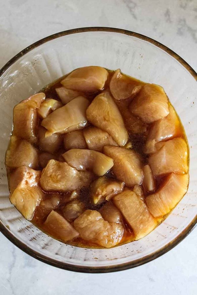 Raw chicken pieces marinating in a glass bowl.