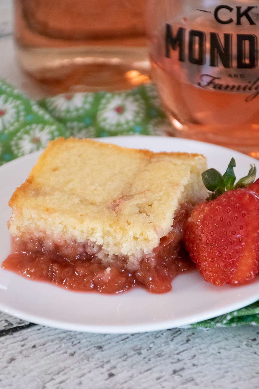 Strawberry Rhubarb Pudding Cake on a white plate with a fresh strawberry to the right.