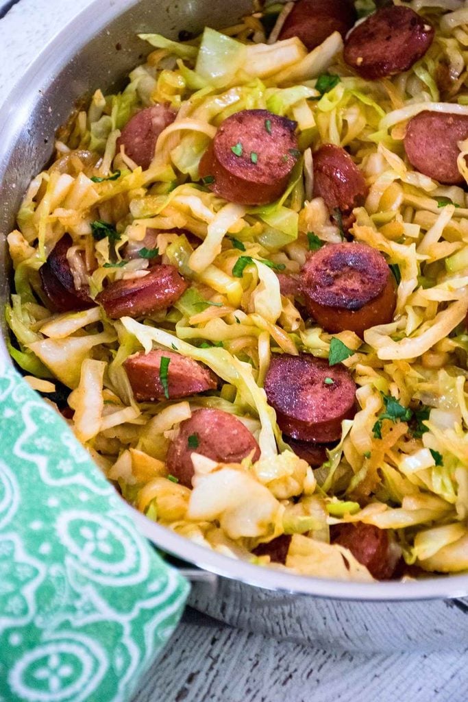 Upclose image of sliced kielbasa and sauteed cabbage in a skillet.